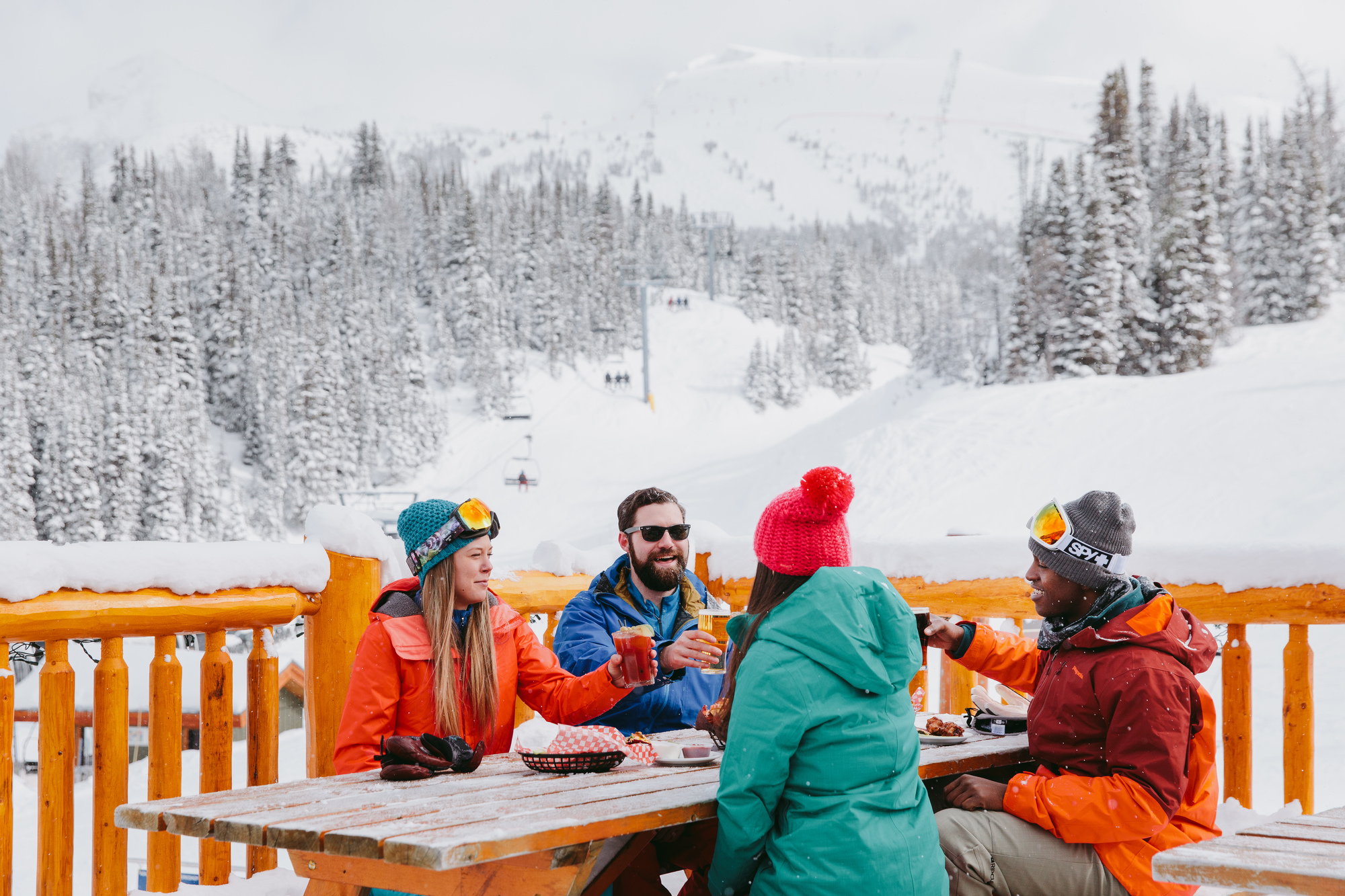 Friends at Mad Trappers enjoying some drinks and appetizers apres ski on an outdoor patio at Sunshine Village in Banff National Park