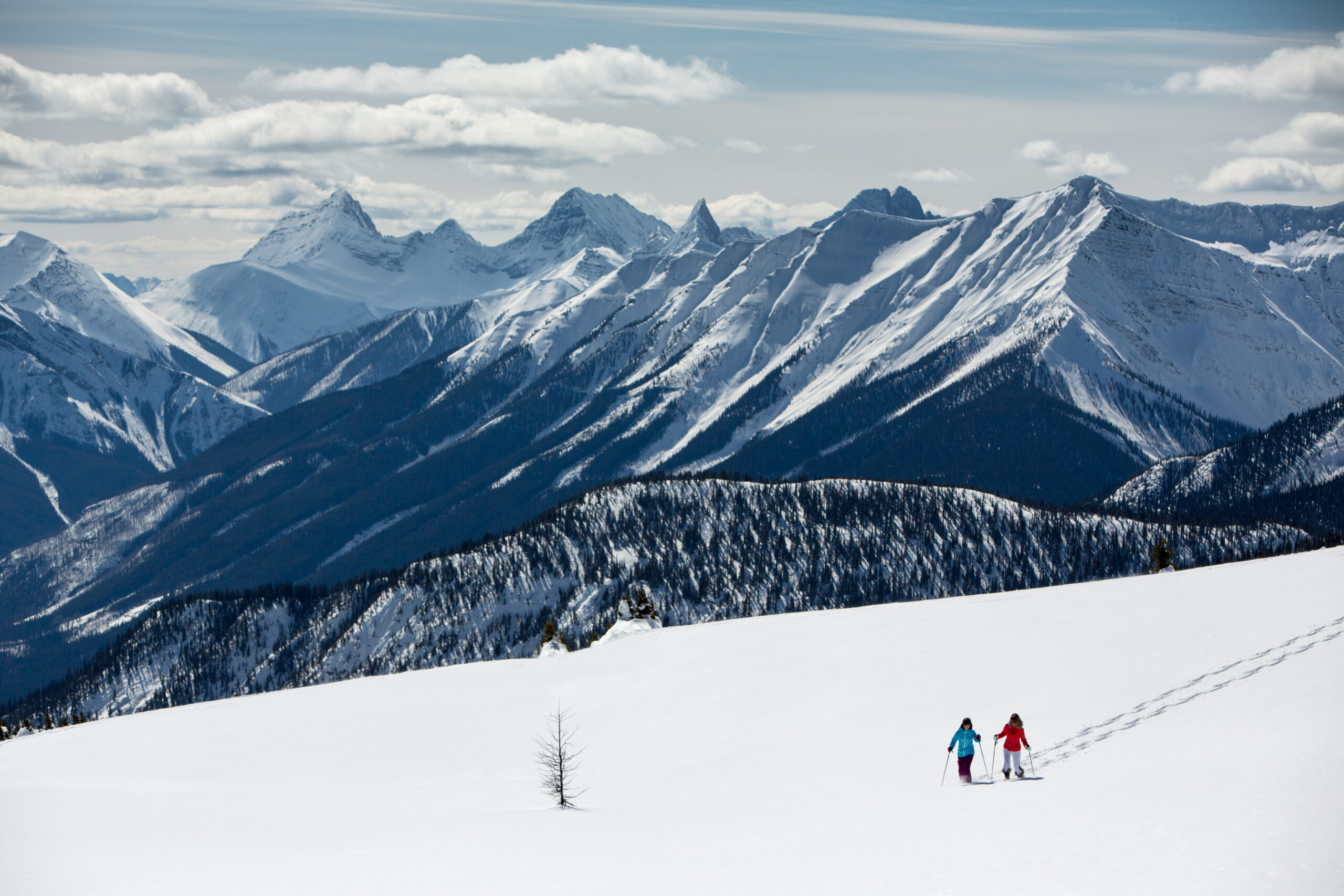 Two people who are snowshoeing in Banff National Park with the mountains in the background