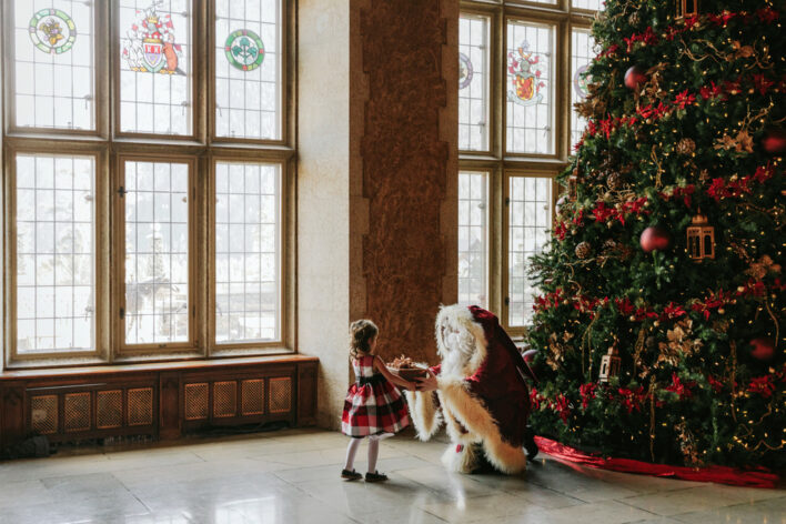 In the Stephen Ballroom Santa is handing a little girl who a present with a fully decorated tree in the background