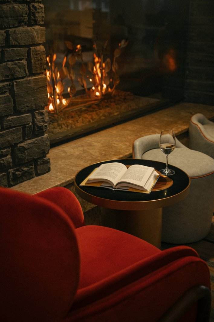Inviting chair with book and glass of wine in front of a fire place at the Fairmont Banff Springs Gold Lounge