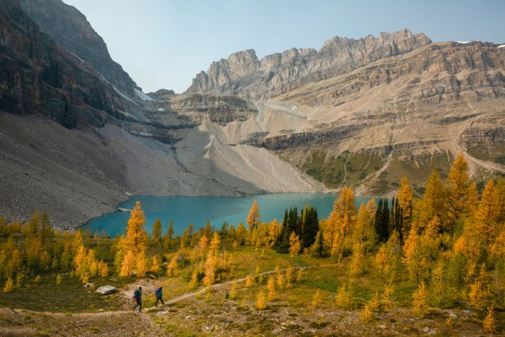 Mountain scenery with a glacier fed lake and larch trees. Two hikers enjoying the day.