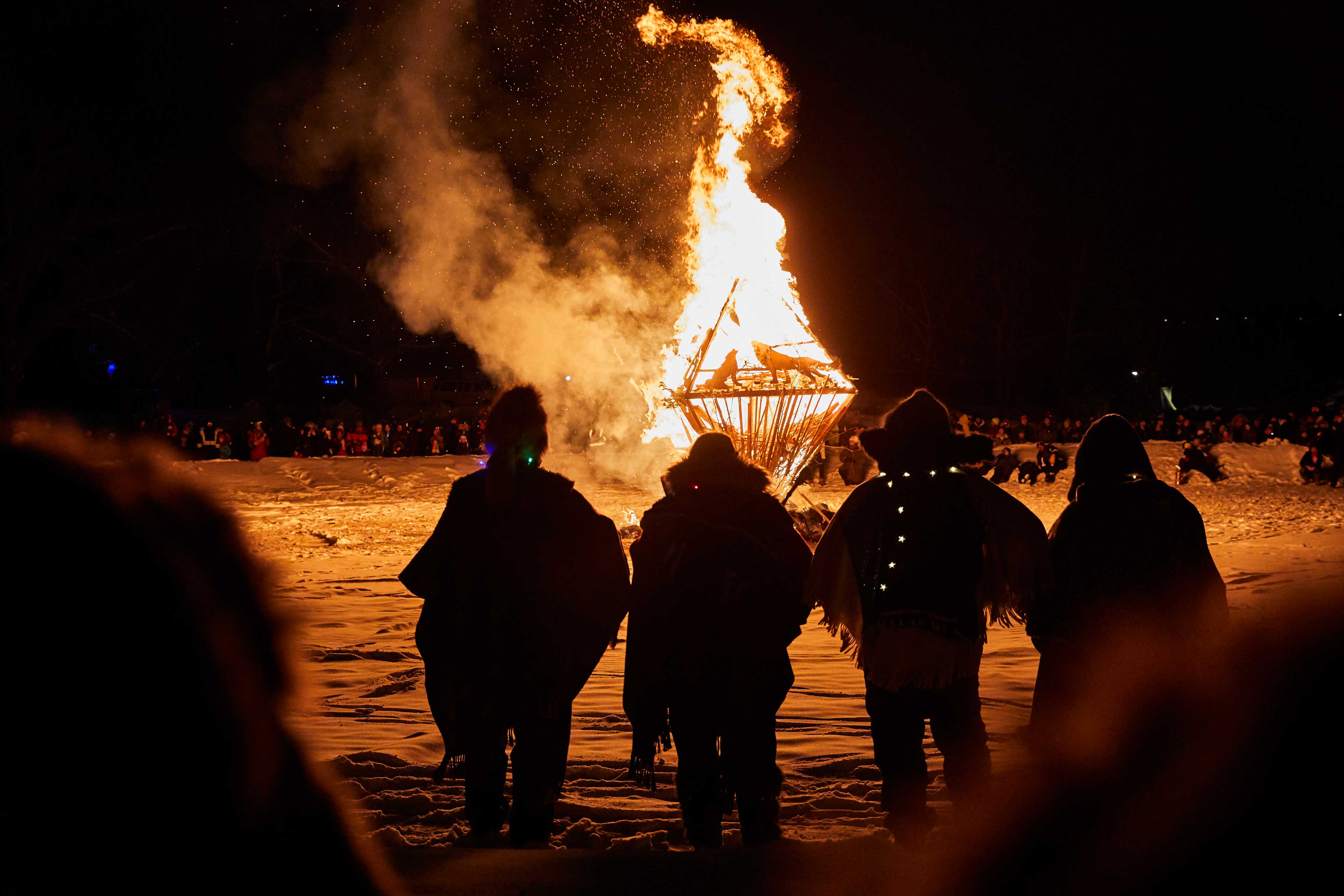 A crowd of people watching a wooden sculpture burn duing the Silver Skate Festival in Edmonton