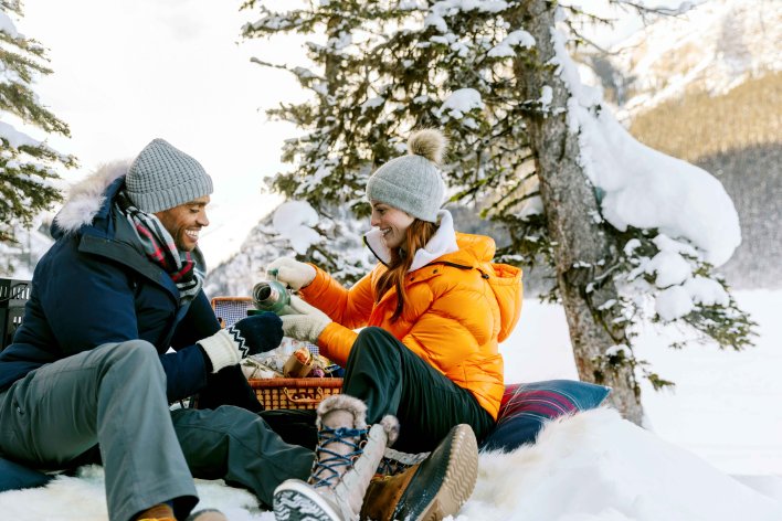 Couple sitting in the snow having a picnic on the edge of Lake Louise