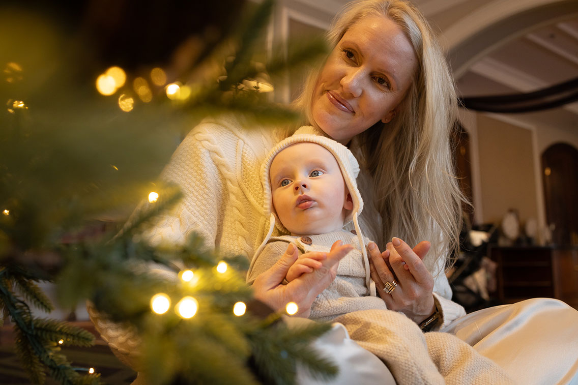 Mother holding her baby beside illuminated holiday greenery at Fairmont Jasper Park Lodge