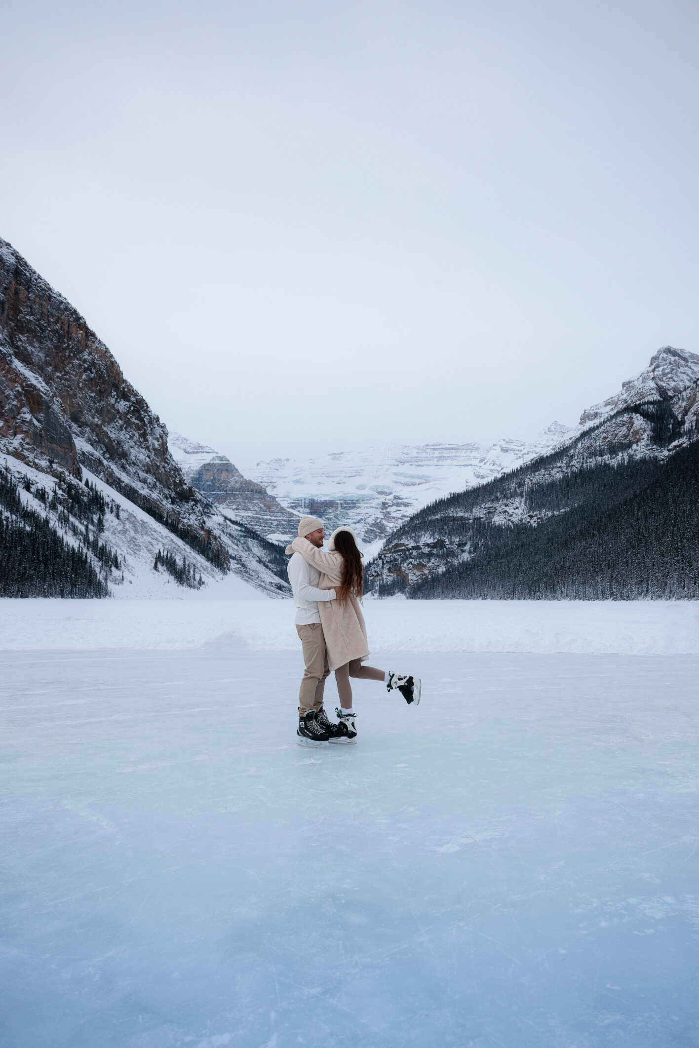Couple ice skating on frozen Lake Louise surrounded by snow-covered mountains