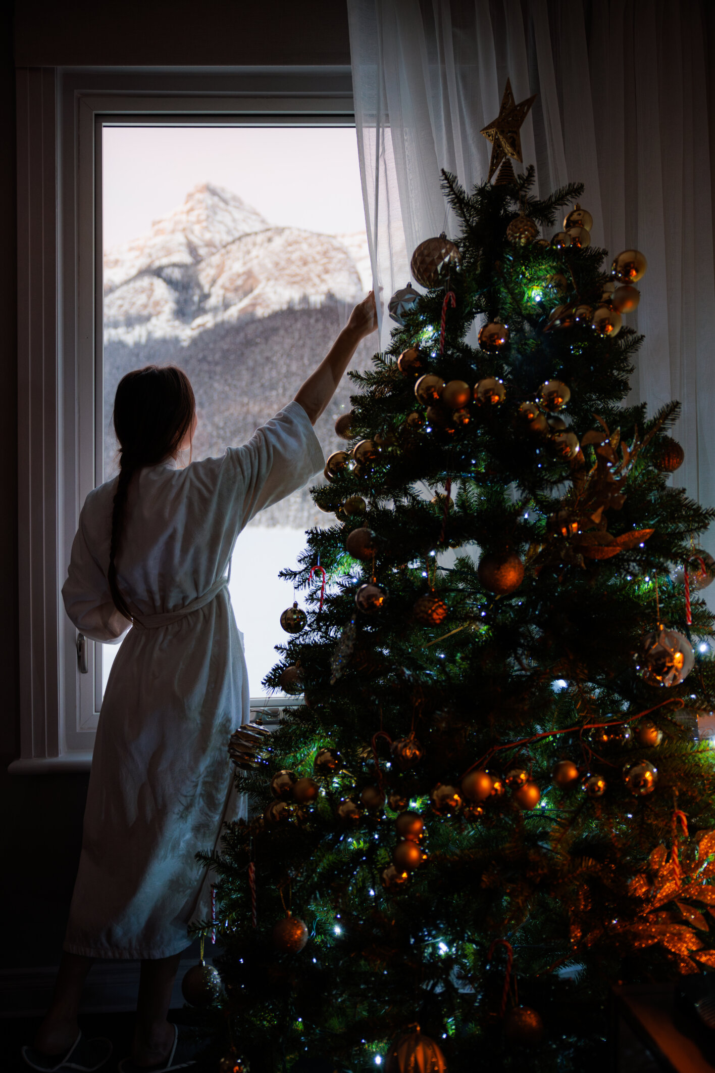 Guest decorating a Christmas tree beside a window overlooking the mountains at Fairmont Chateau Lake Louise
