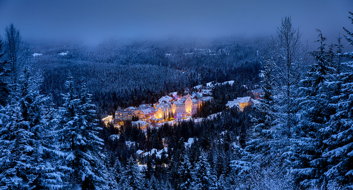 Fairmont Chateau Whistler illuminated at dusk among snow-covered evergreen trees