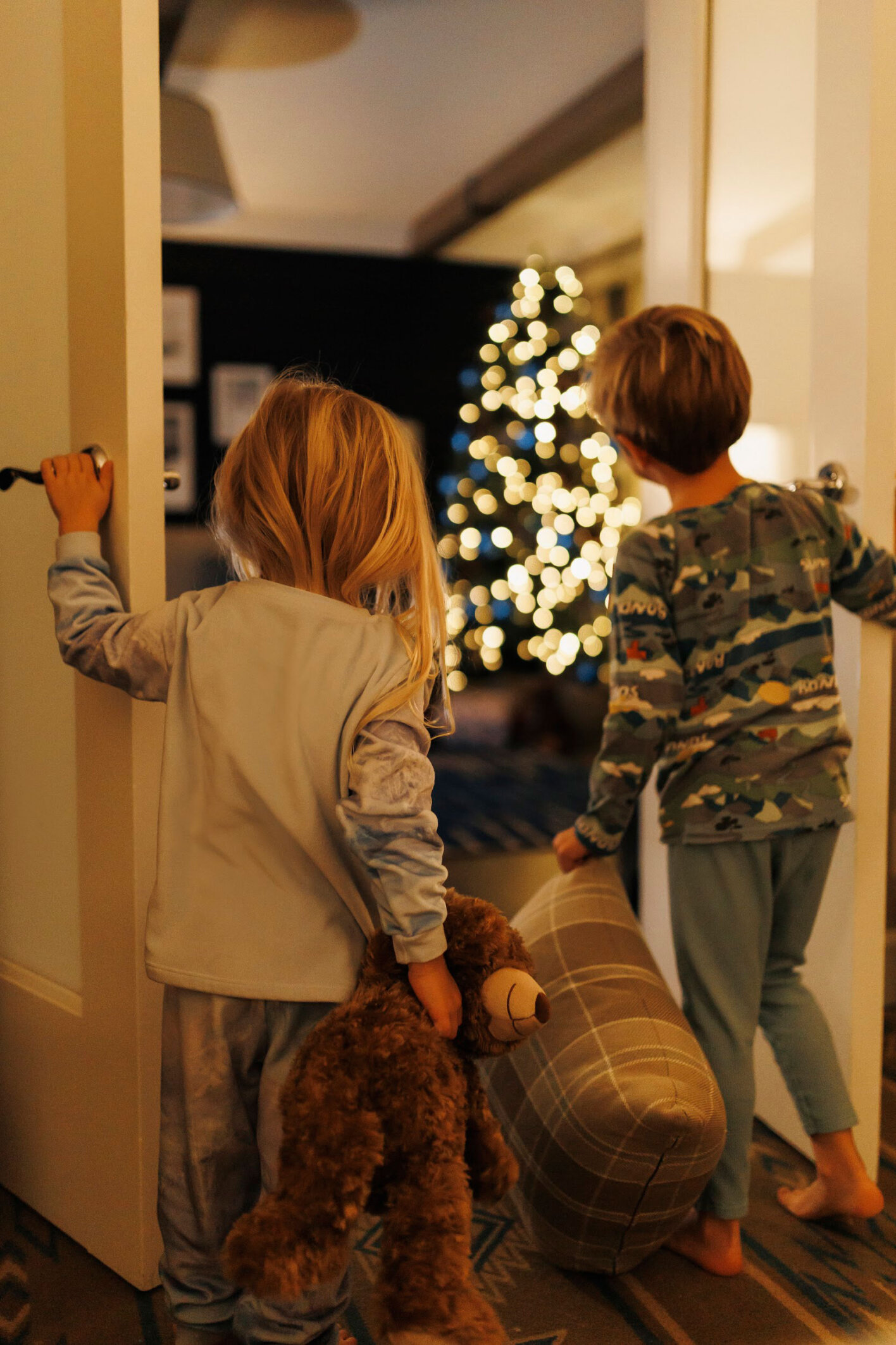 Two children entering a hotel room decorated with a glowing Christmas tree