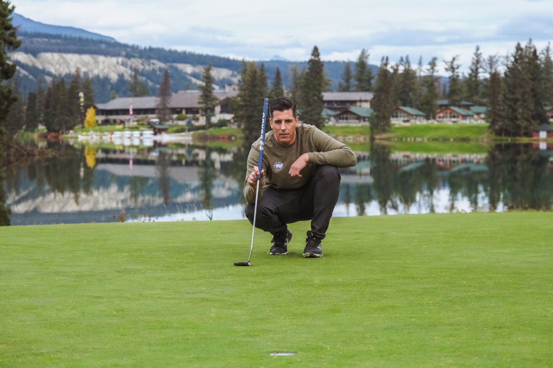 Man crouching to see the line for the putt at Jasper Park Lodge Golf Course